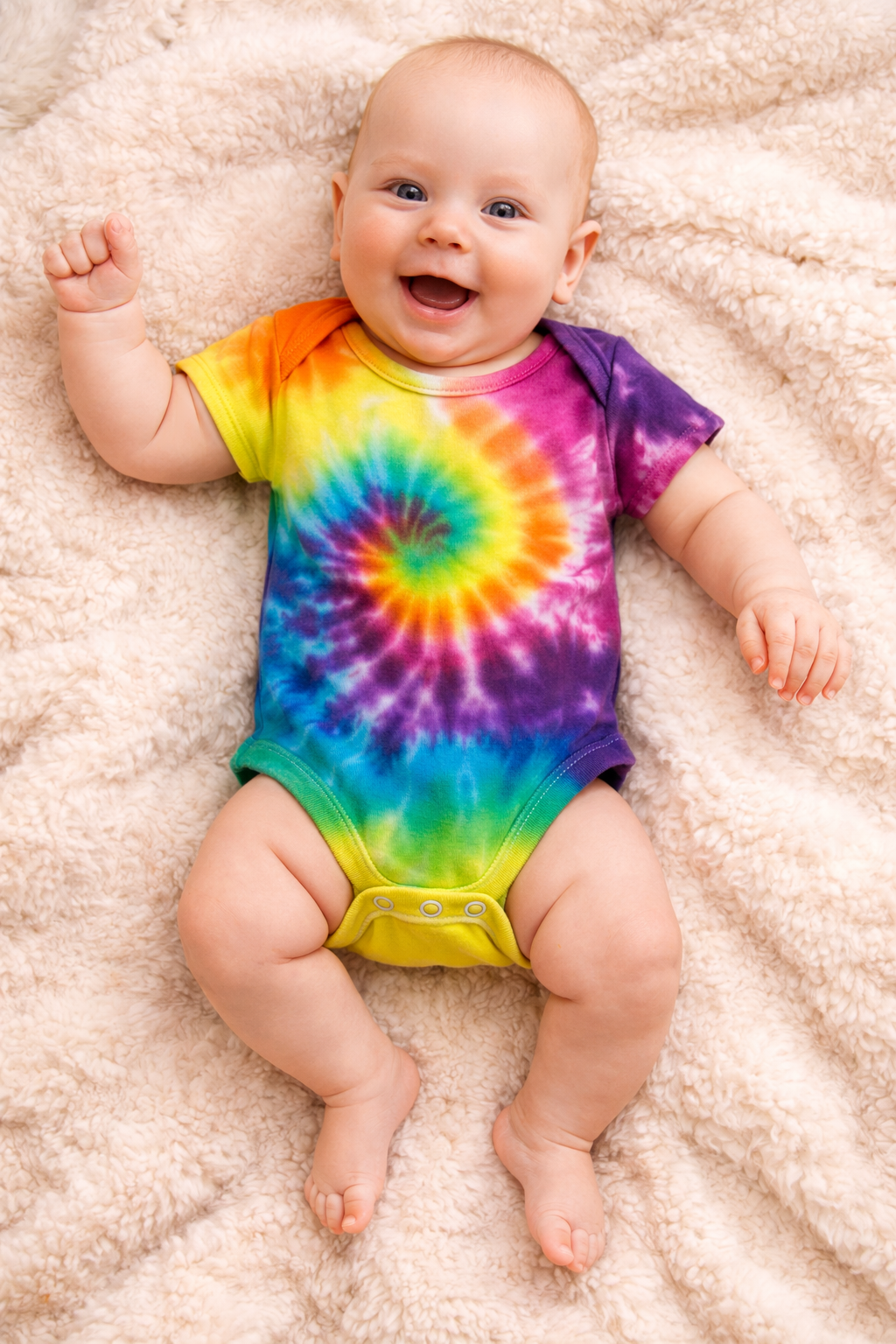 Baby wearing a colorful tie-dye onesie on a soft surface