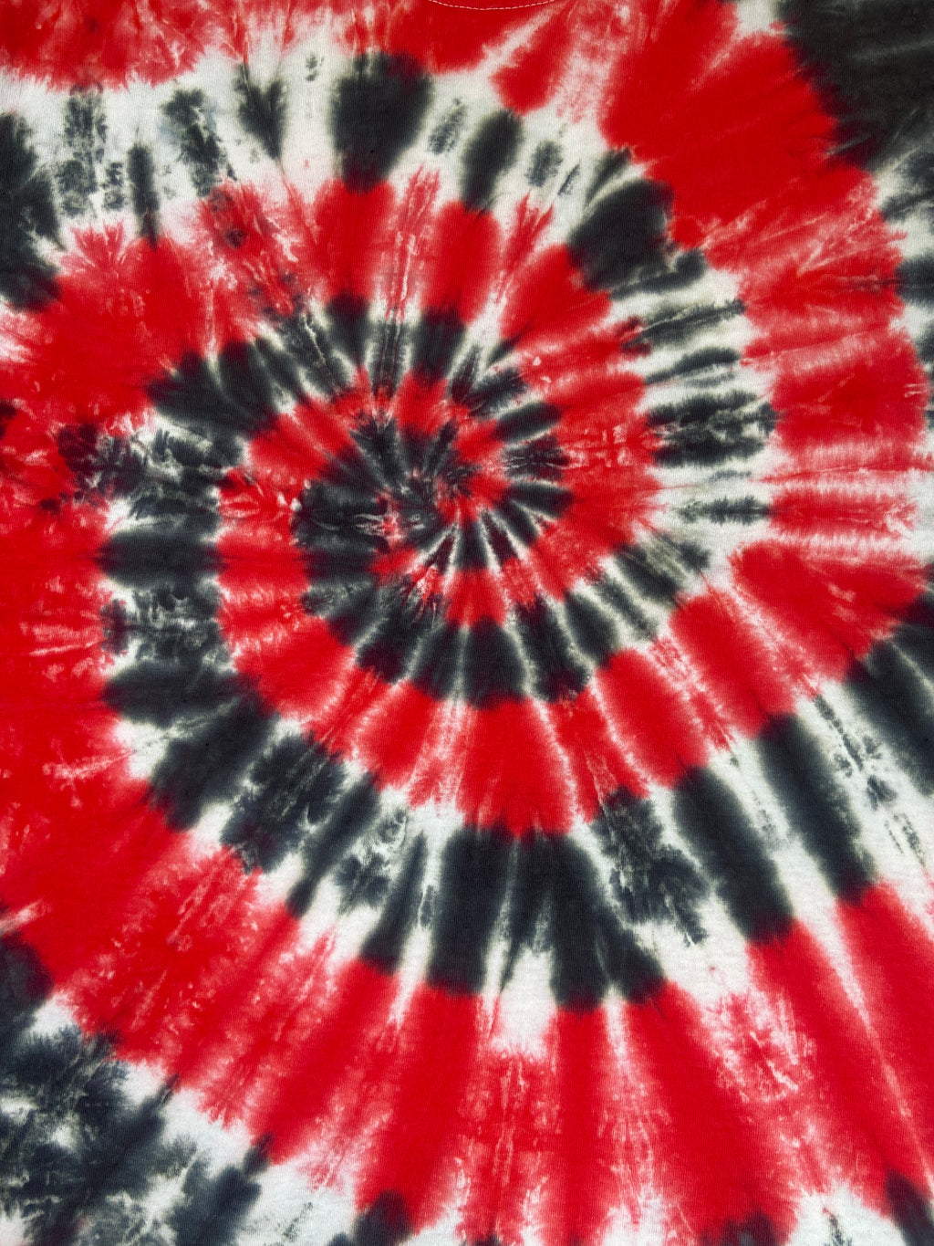 A close-up of a spiral tie-dye pattern in vibrant red, black, and white, showing the fabric texture and color distribution.