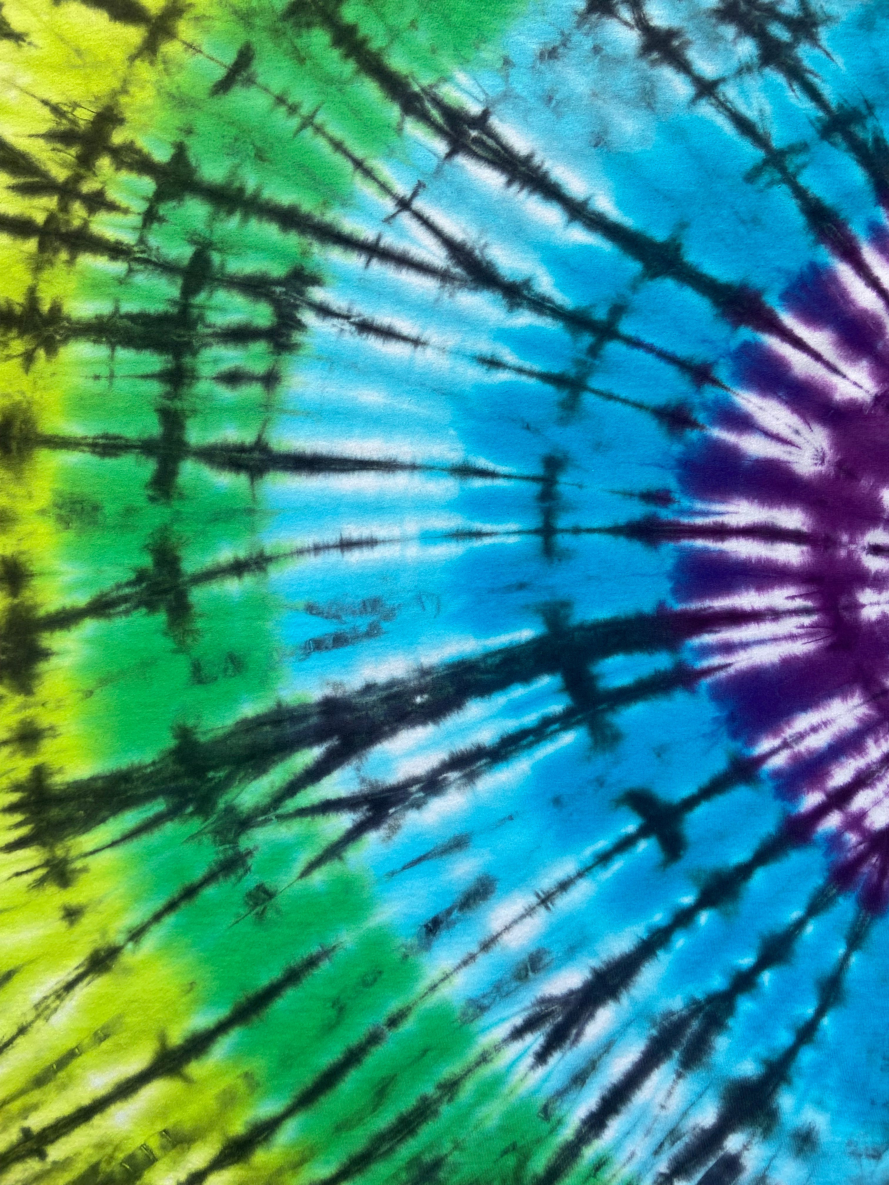 A close-up of a tie-dye pattern with radiating stripes of blue, purple, green, and yellow separated by dark black lines.