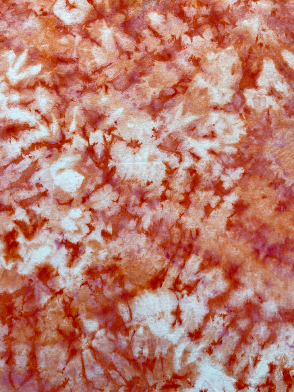 A close-up of a tie-dye pattern featuring mottled shades of terracotta red, rust orange, and off-white.