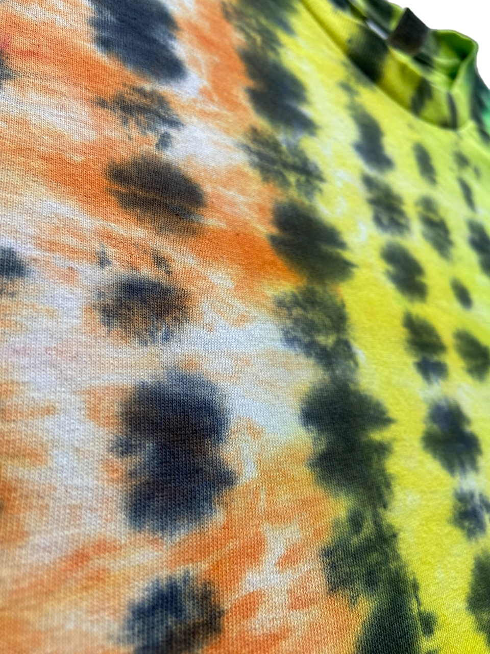 Close-up of a tie-dye fabric with a split design of orange and yellow, both patterned with dark navy spots and streaks.