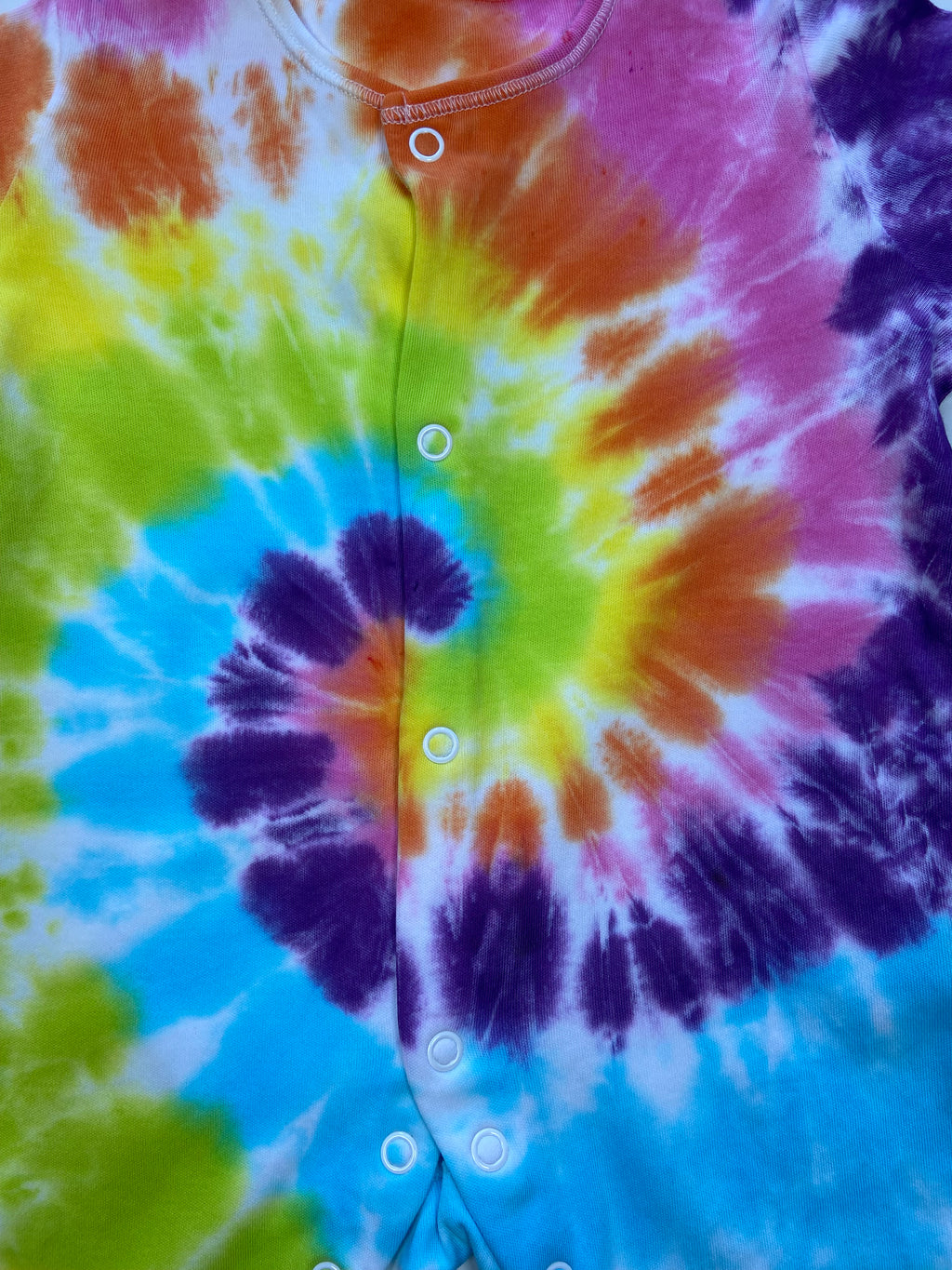 close up of Rainbow spiral tie dye baby sleepsuit in bright blue, green, yellow, orange and purple, hand dyed in the UK by Essex Tie Dye.