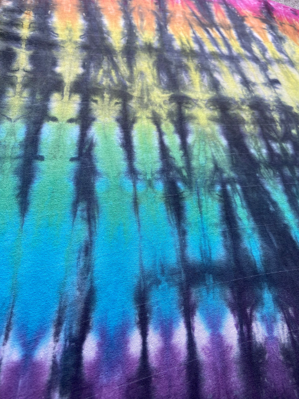 A close-up of a tie-dye fabric with vertical streaks of blue, green, yellow, orange, pink, and purple.