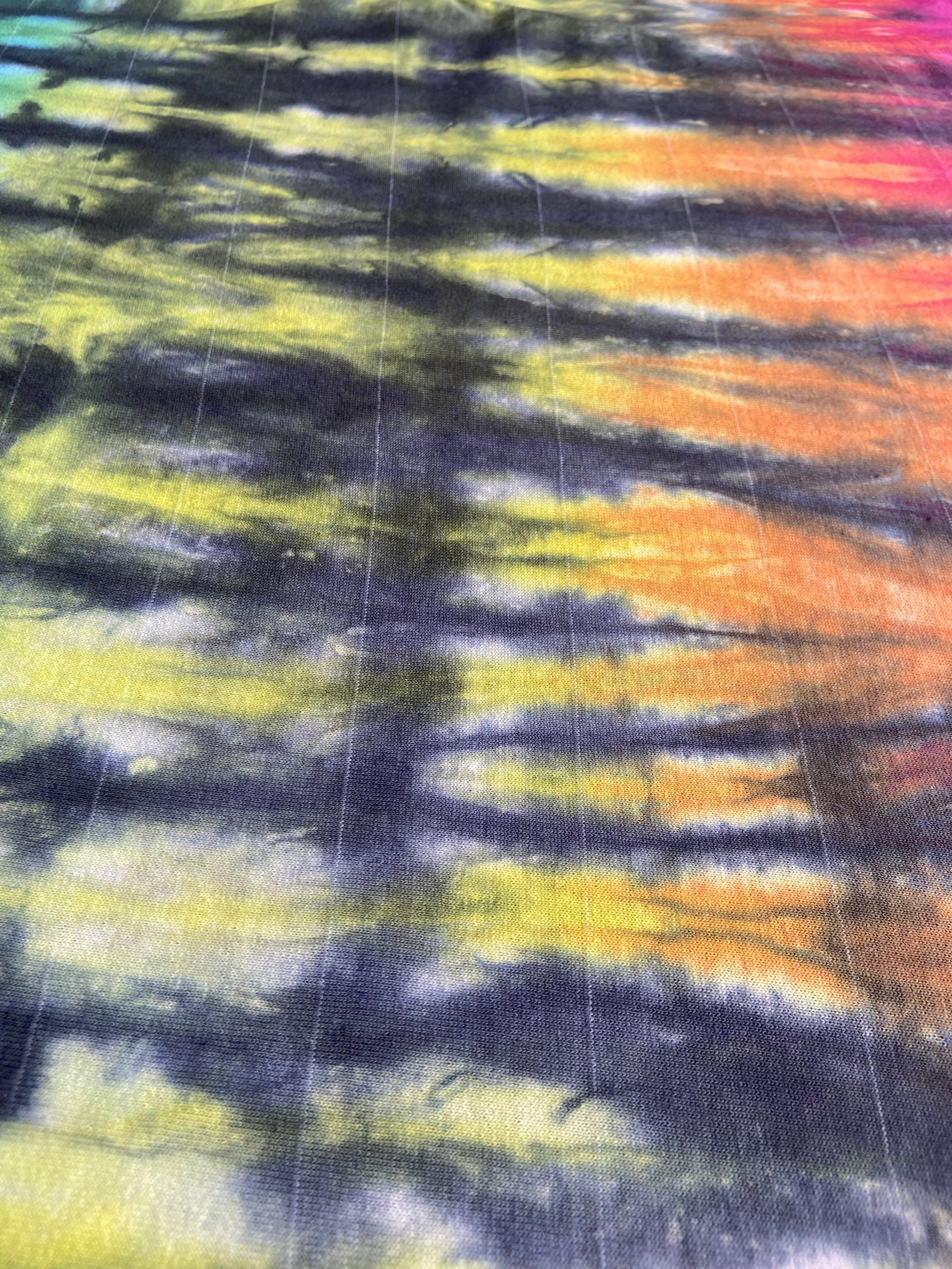 A close-up of a tie-dye fabric with horizontal bands of yellow, orange, purple, and black.