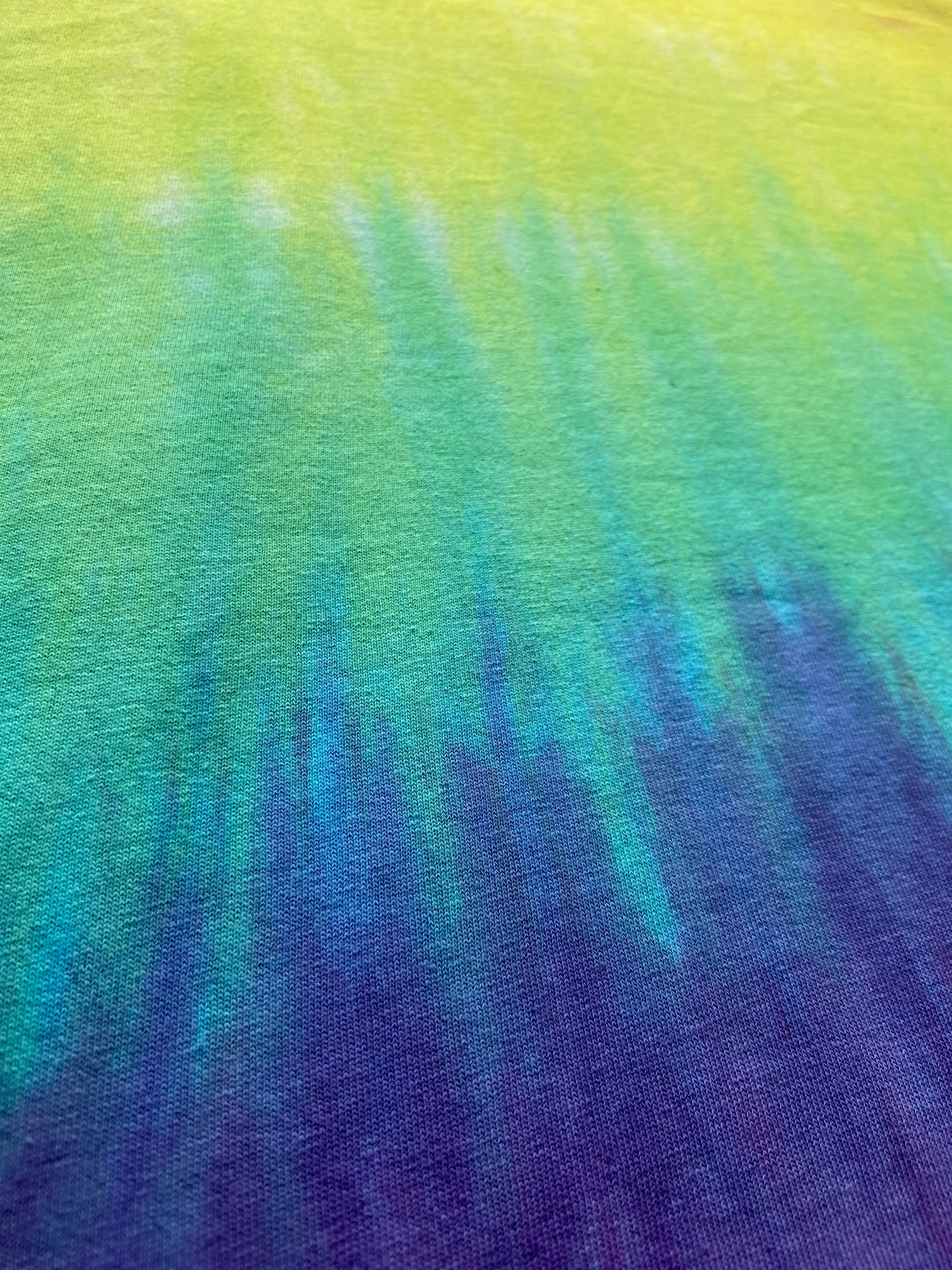 A close-up of a tie-dye fabric with a vertical gradient transitioning from bright yellow-green at the top, through teal and blue, to deep purple at the bottom.