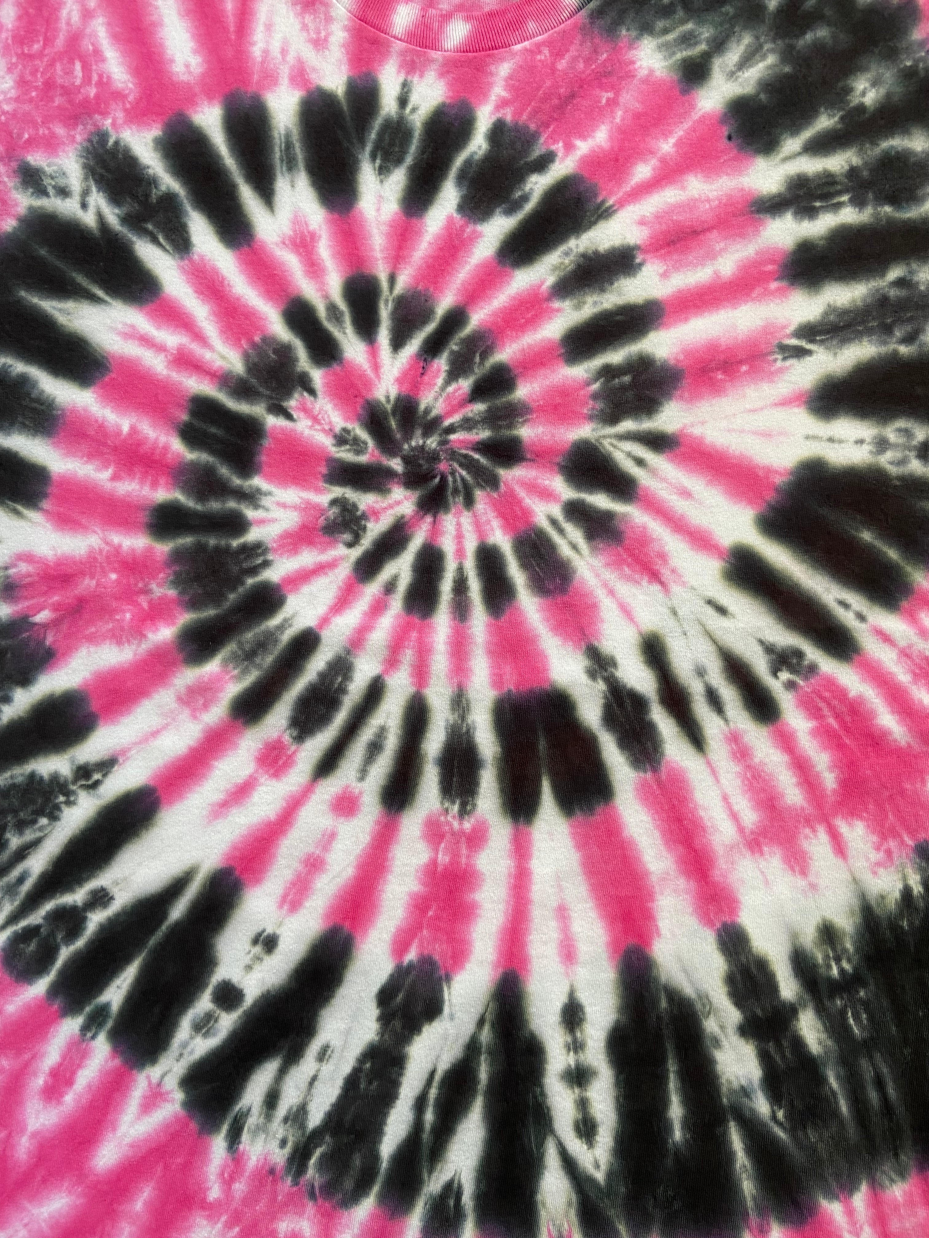 A close-up of a tie-dye spiral pattern featuring vibrant hot pink, black, and white dye streaks radiating from the center.