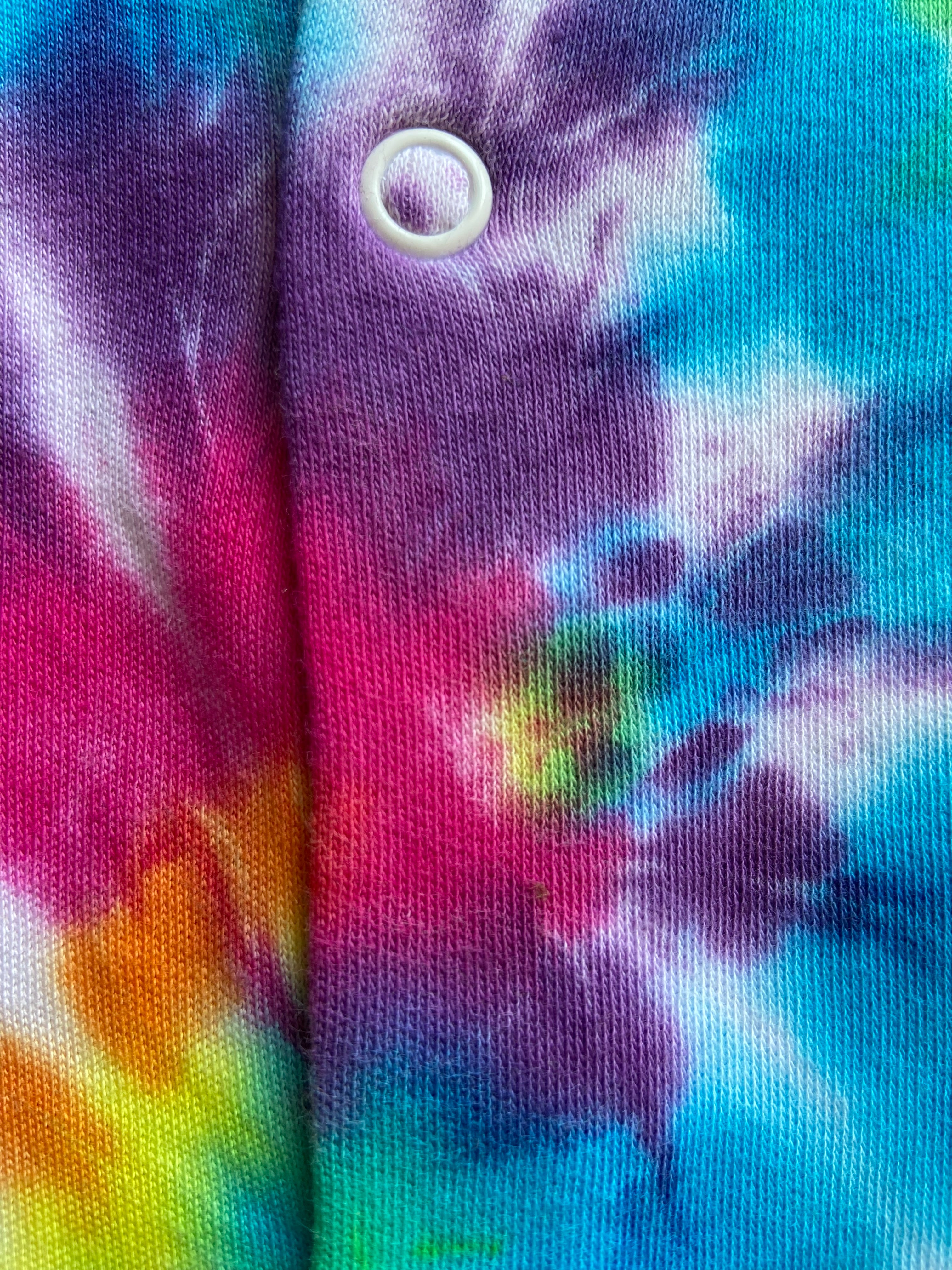 Close-up of tie-dye fabric with a button, featuring a mix of blue, purple, pink, and yellow colors.