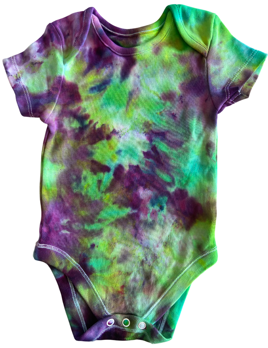 A short-sleeve baby bodysuit with a vibrant green and purple tie-dye pattern, featuring three snap closures at the crotch, shown against a plain white background.