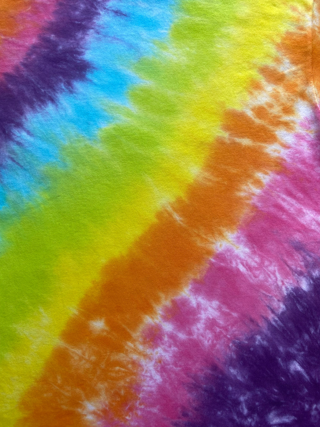 A close-up of a tie-dye fabric with diagonal bands of purple, blue, green, yellow, orange, and pink.