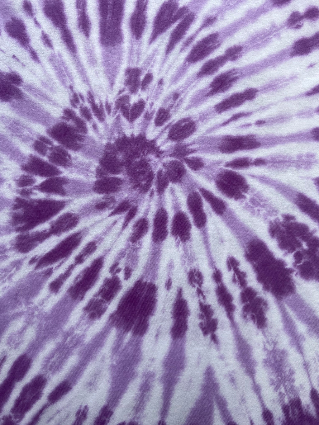 A close-up of a grape and white tie-dye fabric with a spiral burst pattern radiating from the center.