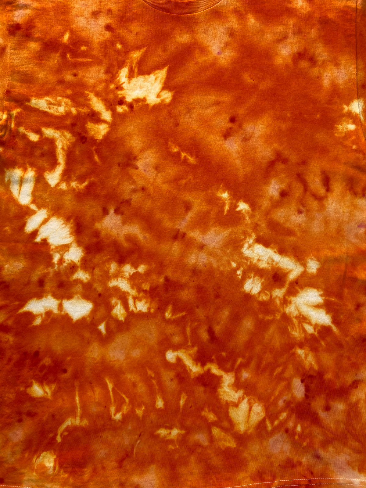 A close-up of a textured orange and brown tie-dye pattern with irregular white and darker orange patches.