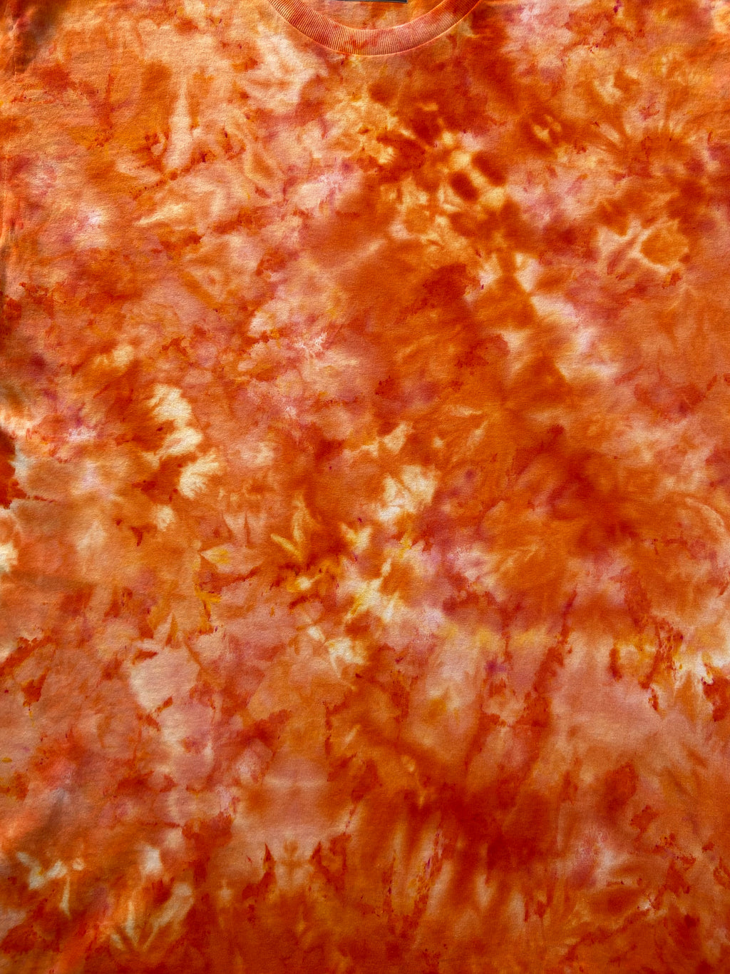 A close-up of a tie-dye fabric with a mottled pattern of orange, red, and light pinkish-beige.