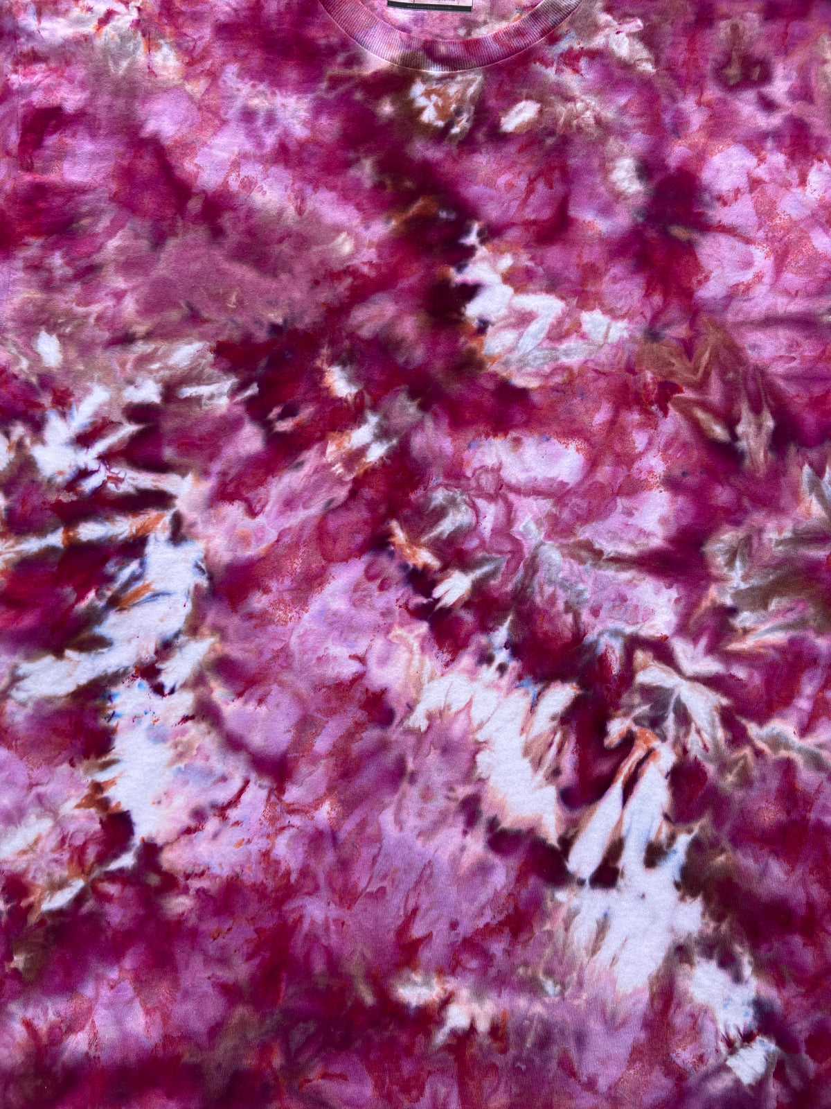 A close-up of a tie-dye fabric pattern featuring marbled swirls of magenta, burgundy, and white.