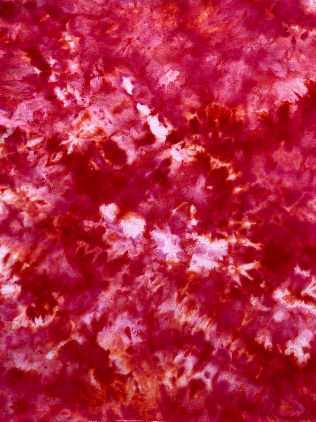 A close-up of a tie-dye fabric pattern featuring mottled shades of deep red, magenta, and light pink.