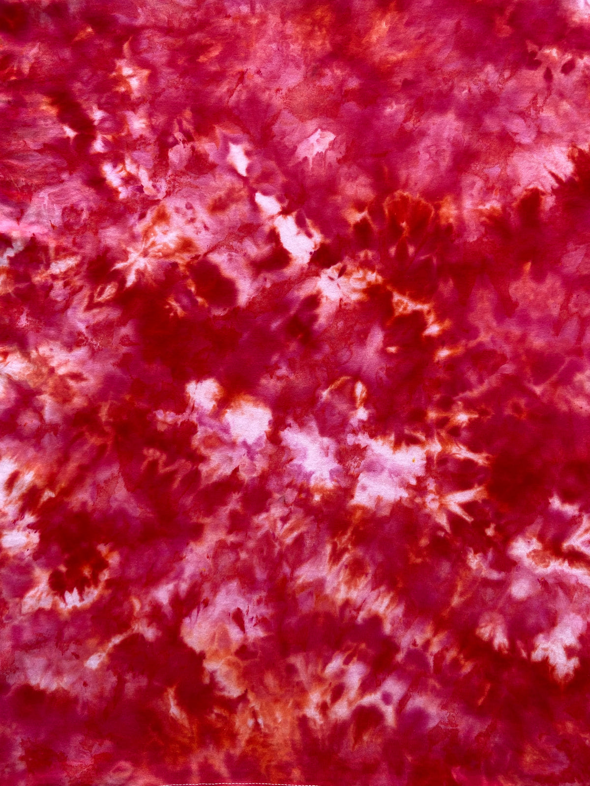 A close-up of a tie-dye fabric pattern featuring mottled shades of deep red, magenta, and light pink.