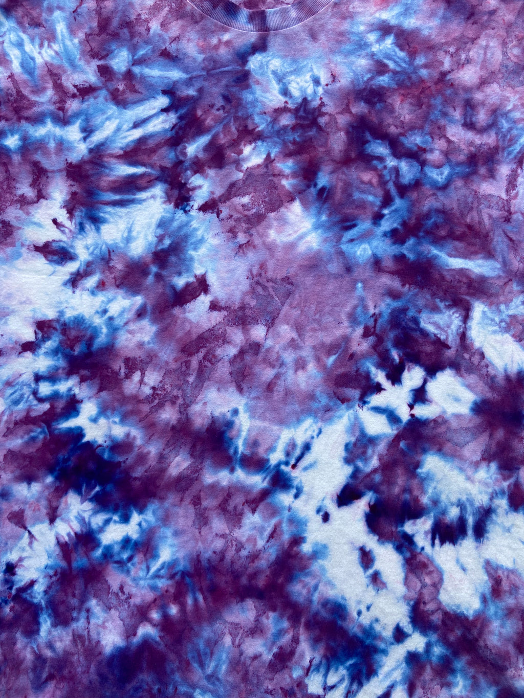 A close-up of a tie-dye fabric pattern featuring a marbled blend of purple, blue, and white.