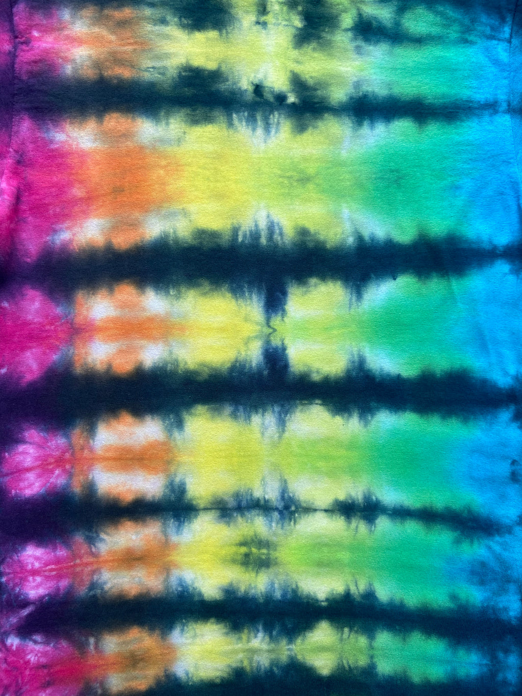 A close-up of a tie-dye fabric with horizontal bands of pink, orange, yellow, green, blue, and dark navy/black tie-dye.