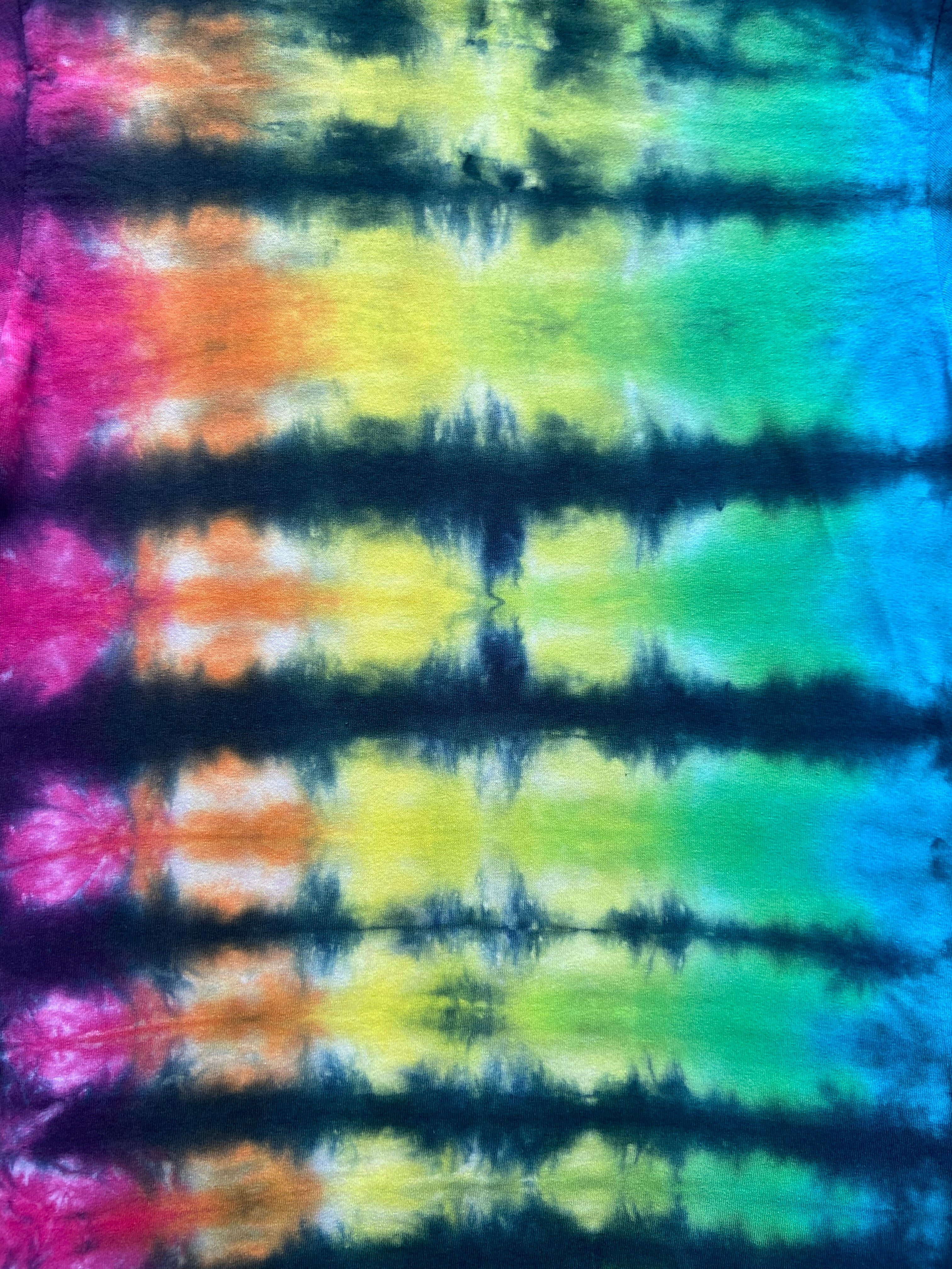 A close-up of a tie-dye fabric with horizontal bands of pink, orange, yellow, green, blue, and dark navy/black tie-dye.