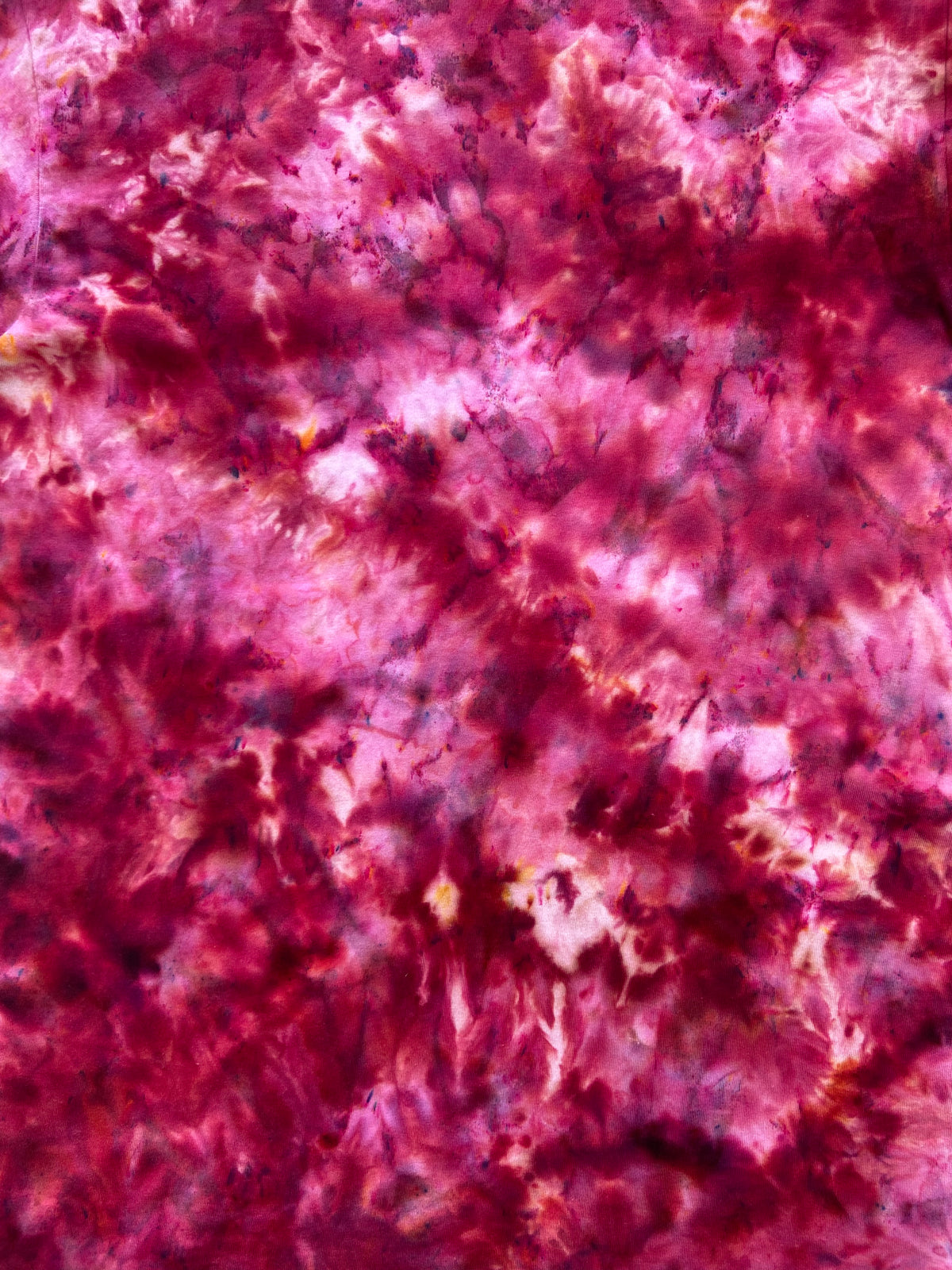 A close-up of a mottled tie-dye fabric pattern in shades of magenta, pink, and deep red with subtle darker marbling.