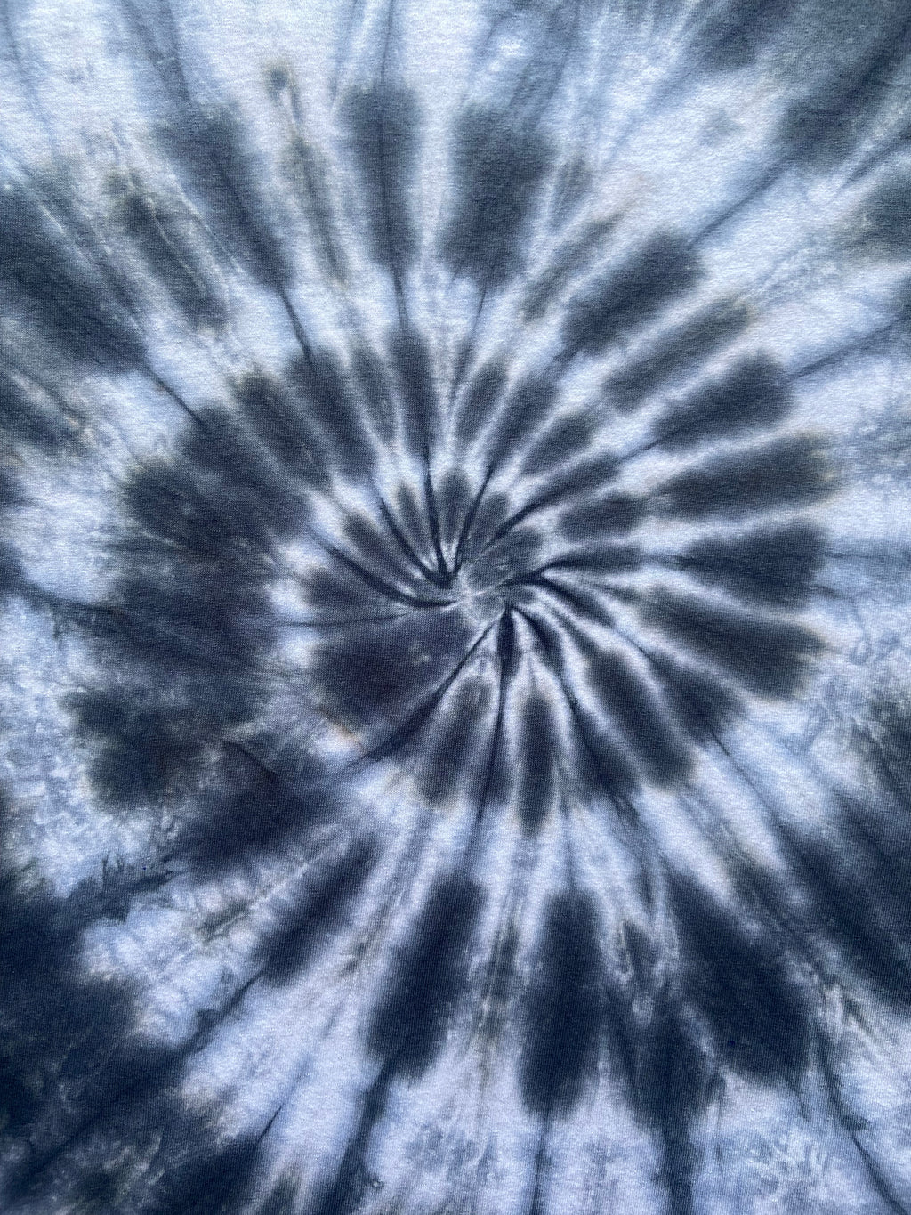 A close-up of a spiral tie-dye pattern in shades of blue, navy, and white, filling the entire frame.