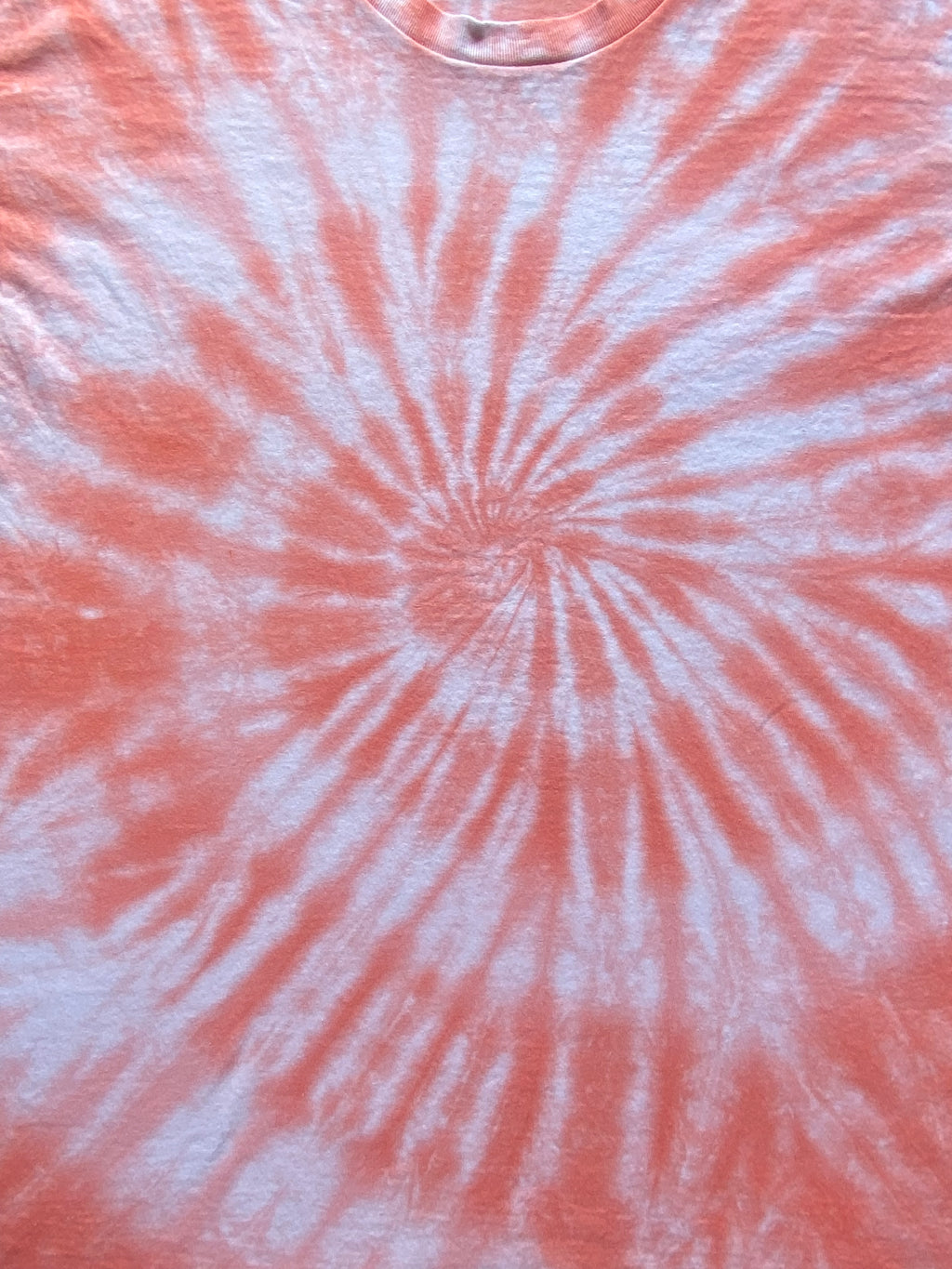 A close-up of a tie-dye t-shirt featuring a spiral pattern in coral pink and white.