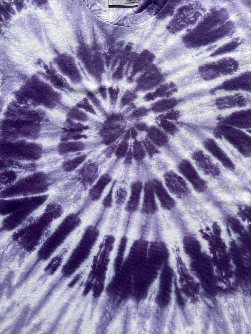 A close-up of a tie-dye t-shirt featuring a spiral pattern in shades of purple and white.