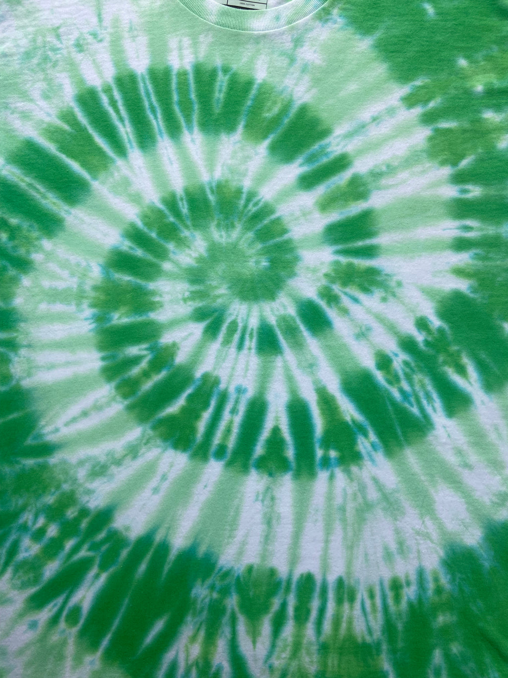 A close-up of a green and white tie-dye spiral pattern on a fabric surface.