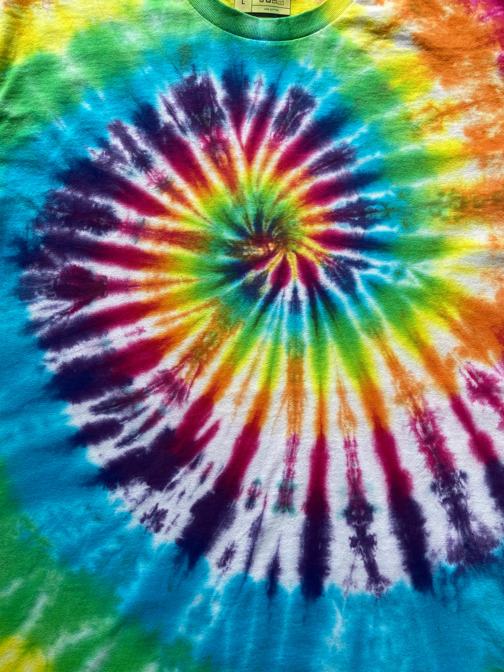 A close-up of a tie-dye t-shirt featuring a vibrant spiral pattern with blue, green, yellow, orange, red, and purple colors radiating from the center.