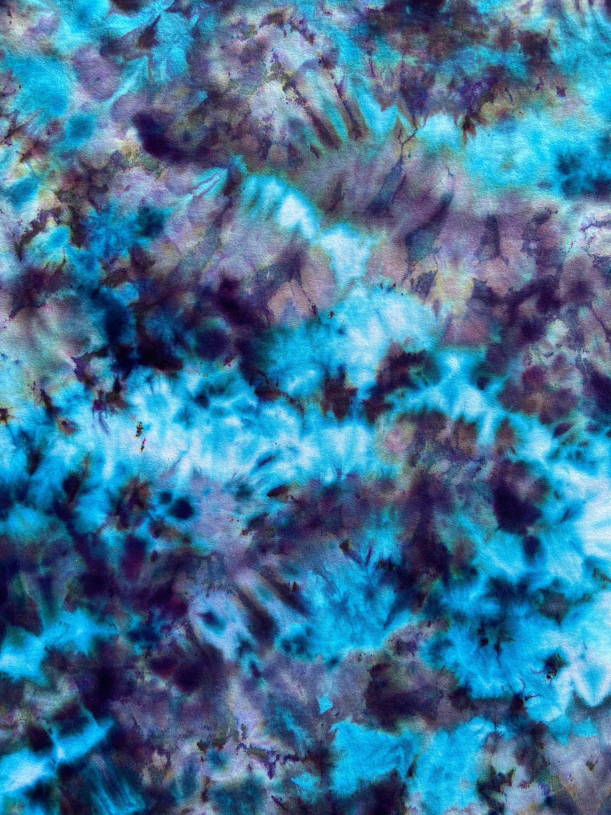 Close-up of The Alchemist Ice Scrunch tie dye fabric showing electric blue, turquoise, violet and dark charcoal tones with intricate crystalline patterns.