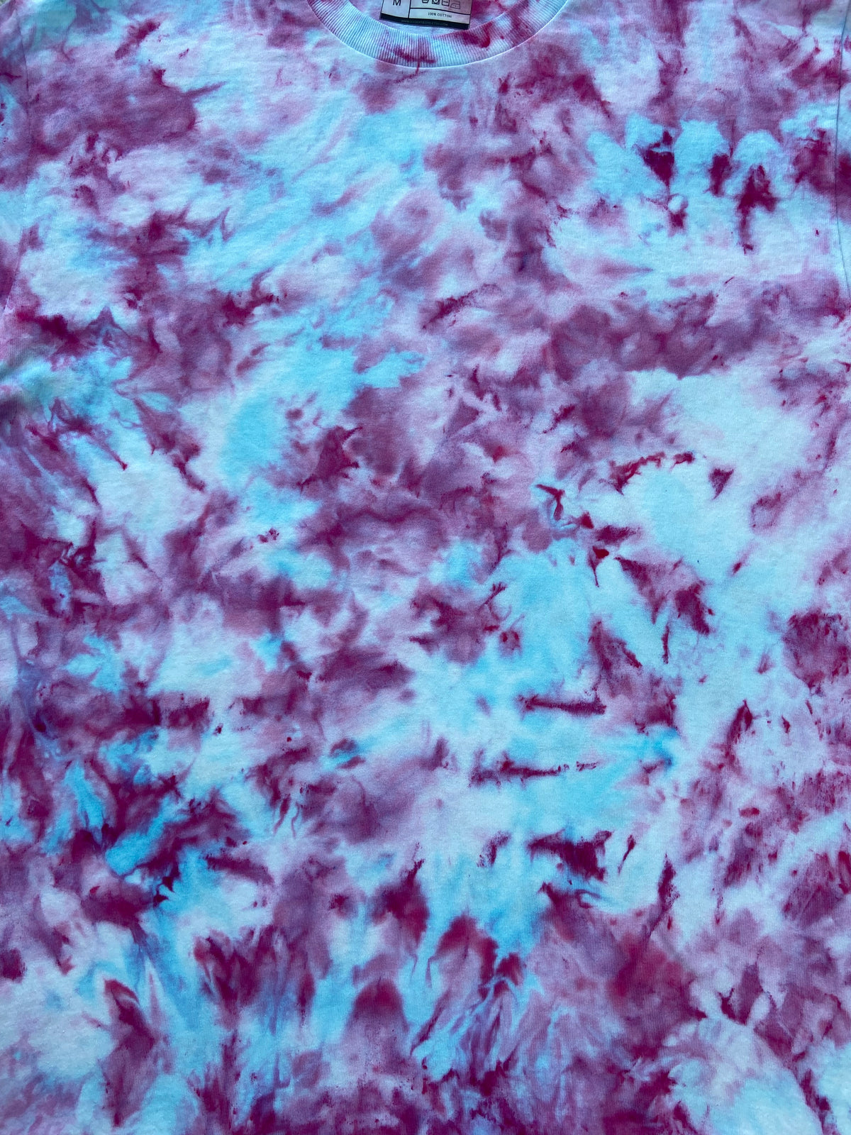 A close-up of a tie-dye t-shirt fabric featuring a marbled pattern of light blue, purple, and white.