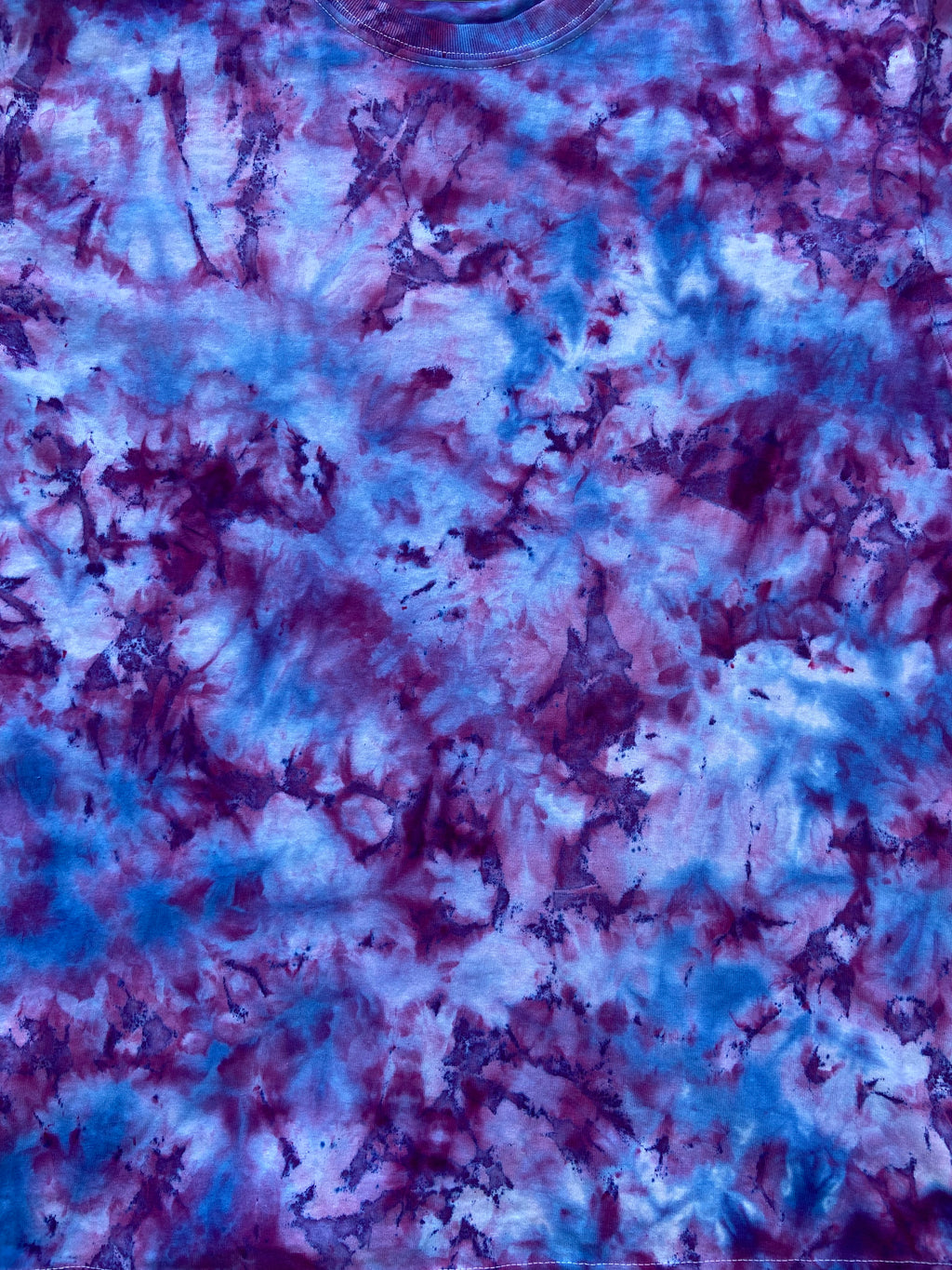 A close-up of a tie-dye fabric pattern featuring a marbled blend of blue, purple, and pink hues.