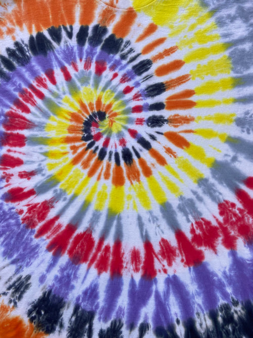 A close-up of a tie-dye spiral pattern on a garment, featuring concentric rings of orange, yellow, red, purple, black, and gray on a white base.