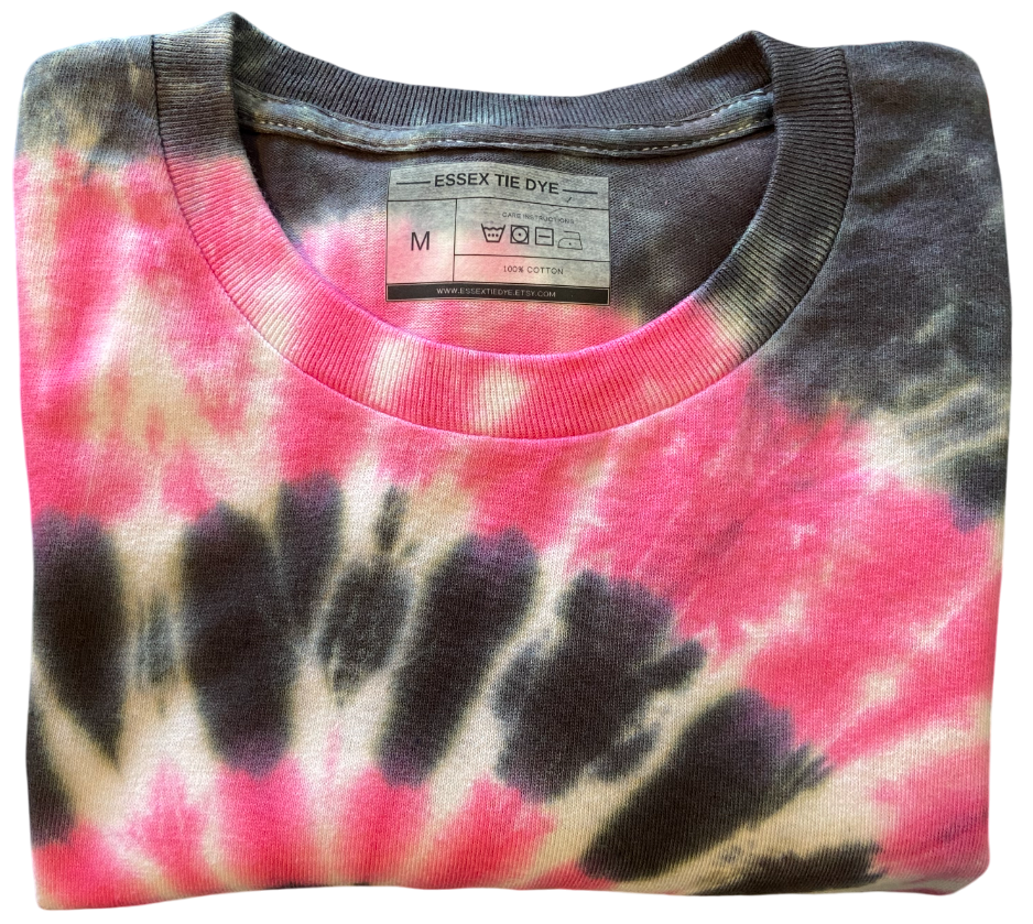A folded crewneck t-shirt featuring a pink, black, and beige spiral tie-dye pattern, with the brand label 'ESSEX TIE DYE' visible inside the collar.