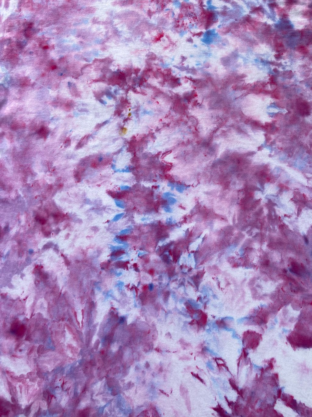 A close-up of a tie-dye pattern featuring swirling shades of magenta pink, purple, and light blue on a white base.